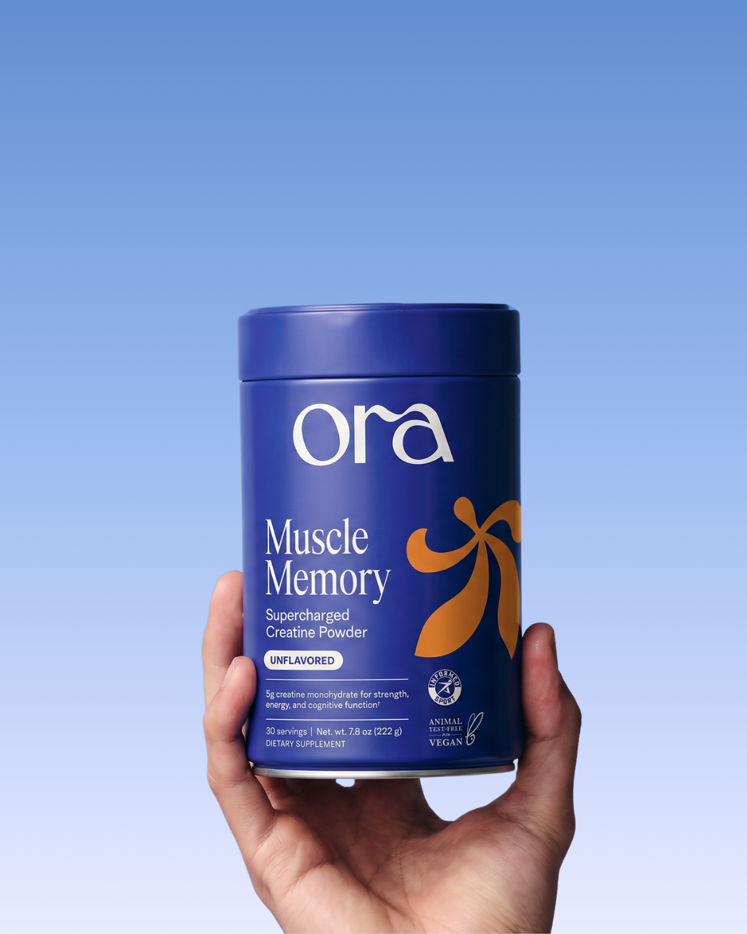 A hand holds a blue tub of Ora Muscle Memory Supercharged Creatine Powder against a blue background.