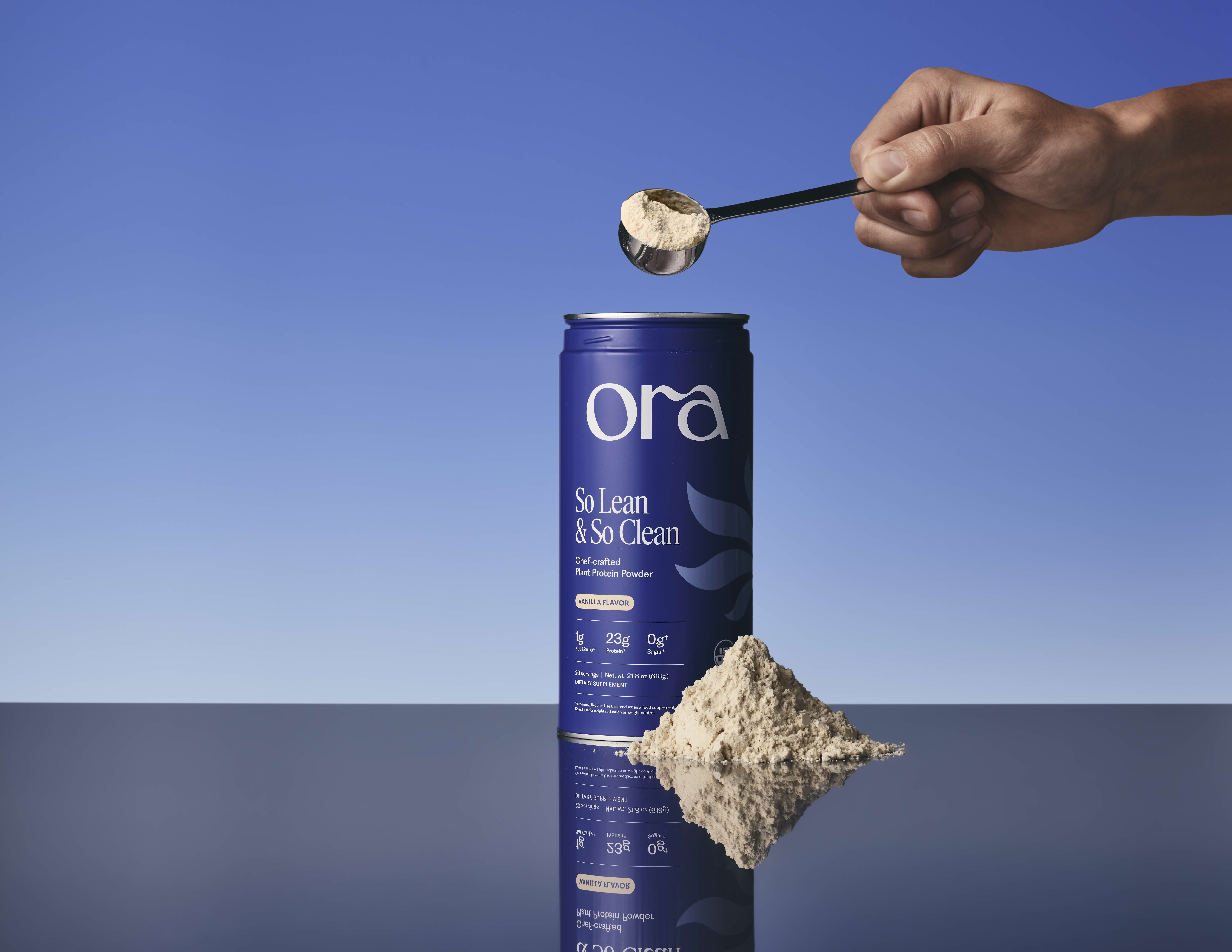 Hand holding a scoop of protein powder above a blue canister and a pile of powder.