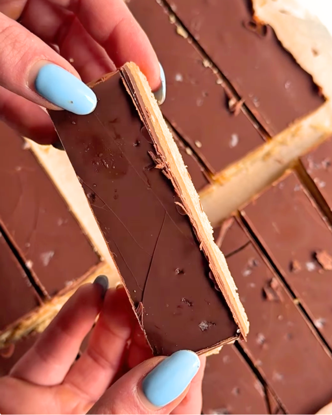 Person holding a chocolate-covered layered pastry slice over a platter.