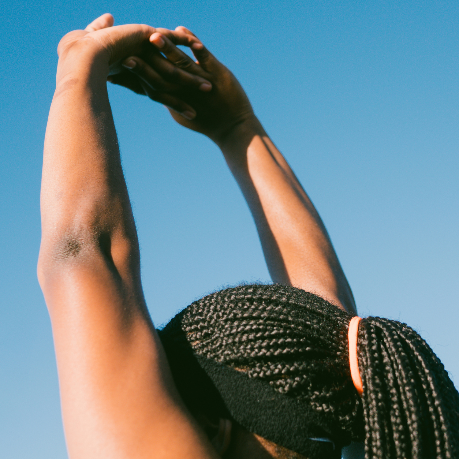 Person stretching arms upward against a clear blue sky.