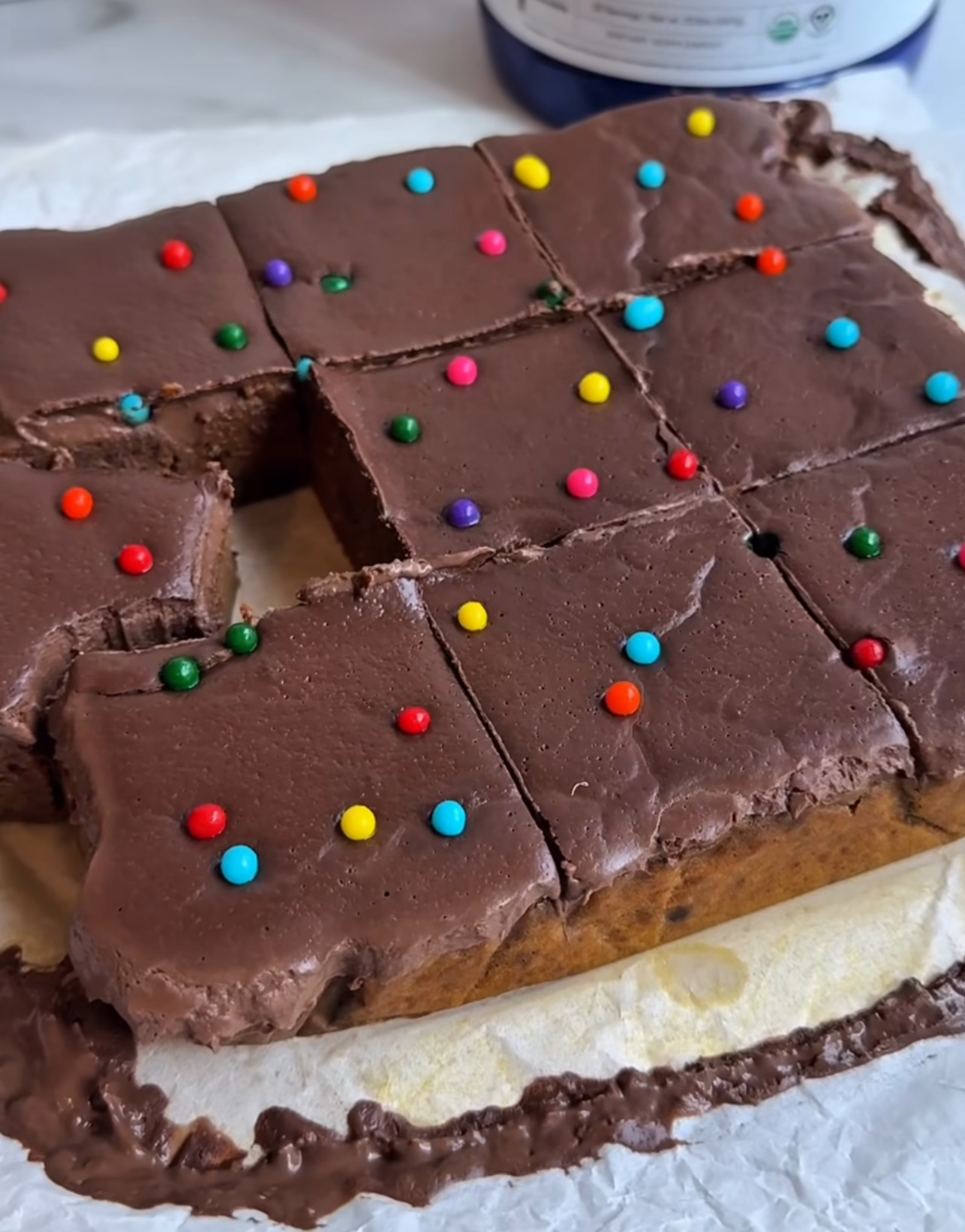Chocolate frosted cake slices with colorful sprinkles on parchment paper.