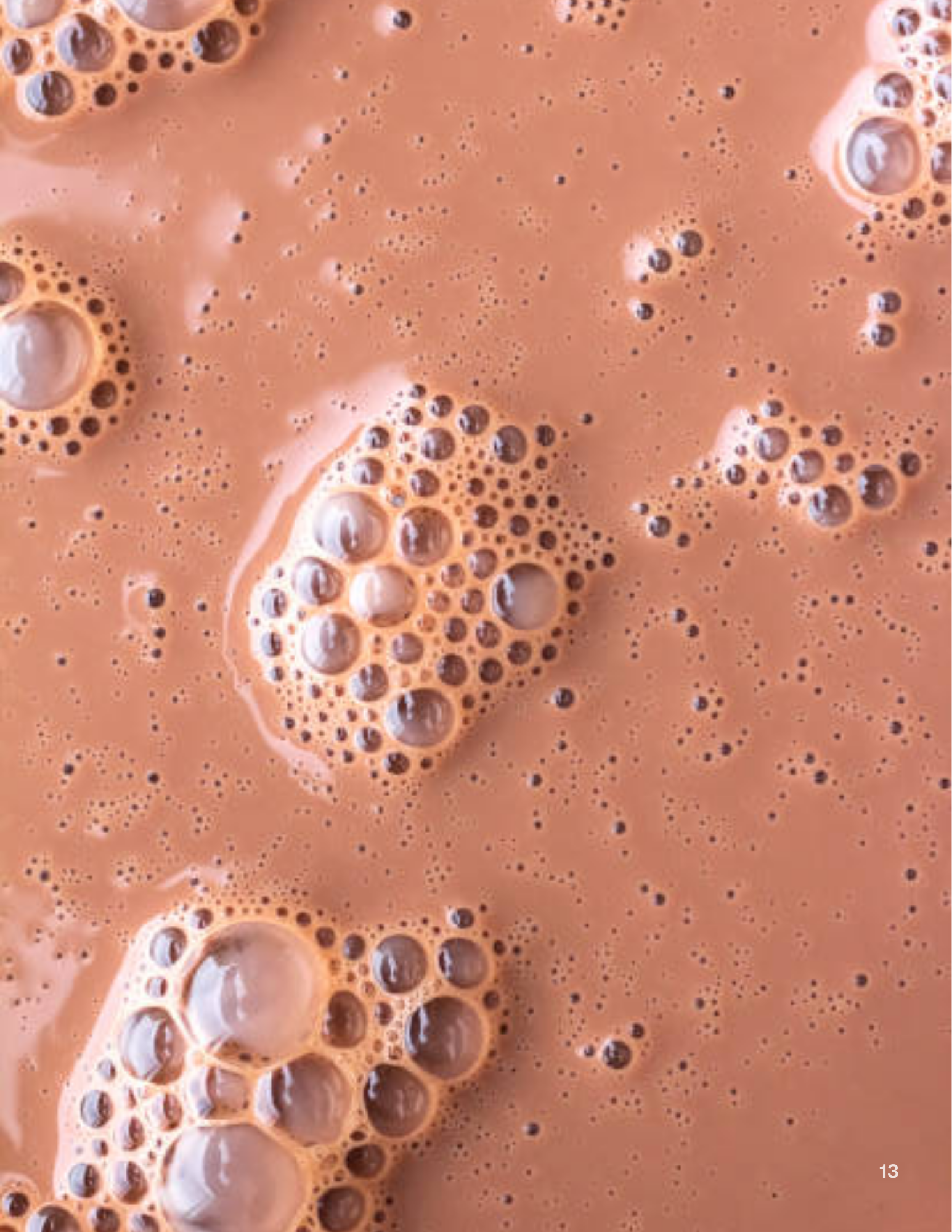 A close-up, top-down view of a bubbly, light-brown liquid, possibly chocolate milk.