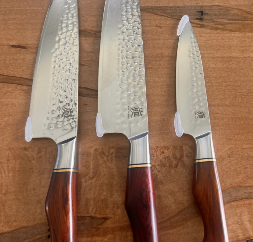 Three chef knives with wooden handles on a wooden surface.