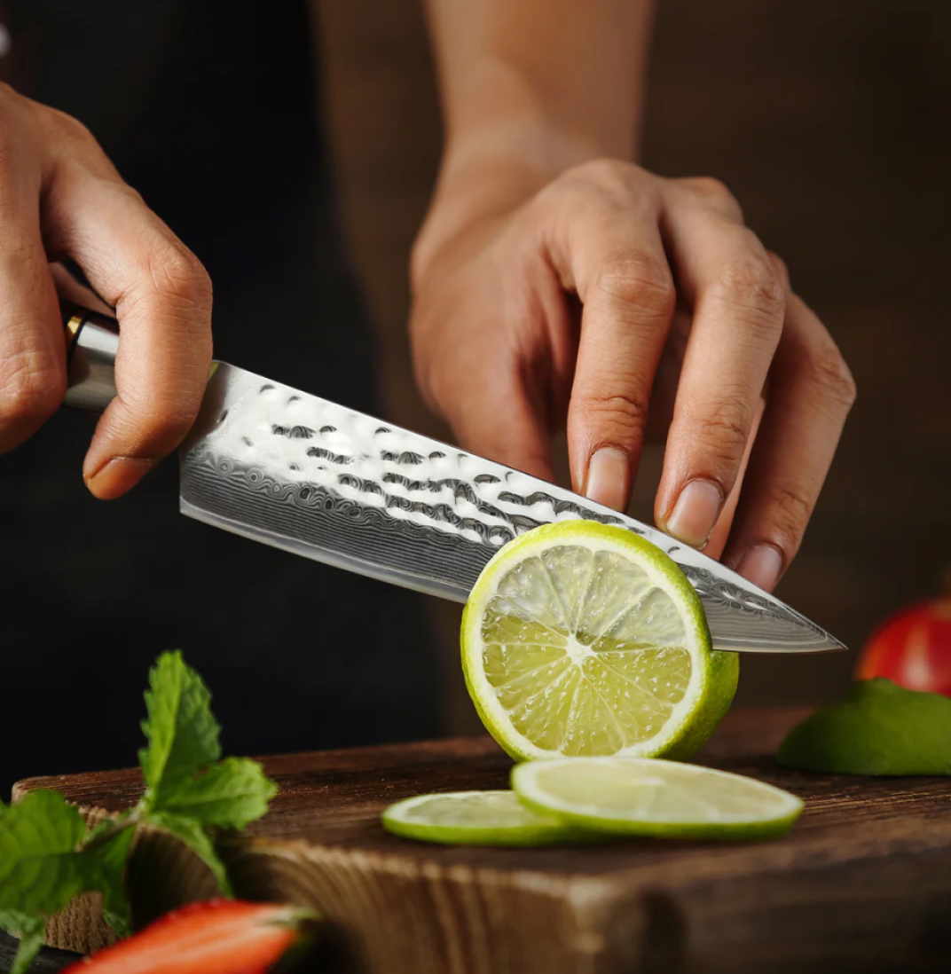 Person slicing a lime with a knife on a wooden board.