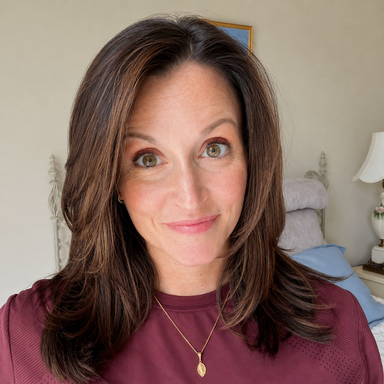 A smiling woman with shoulder-length brown hair and hazel eyes, wearing a maroon shirt and a gold necklace.