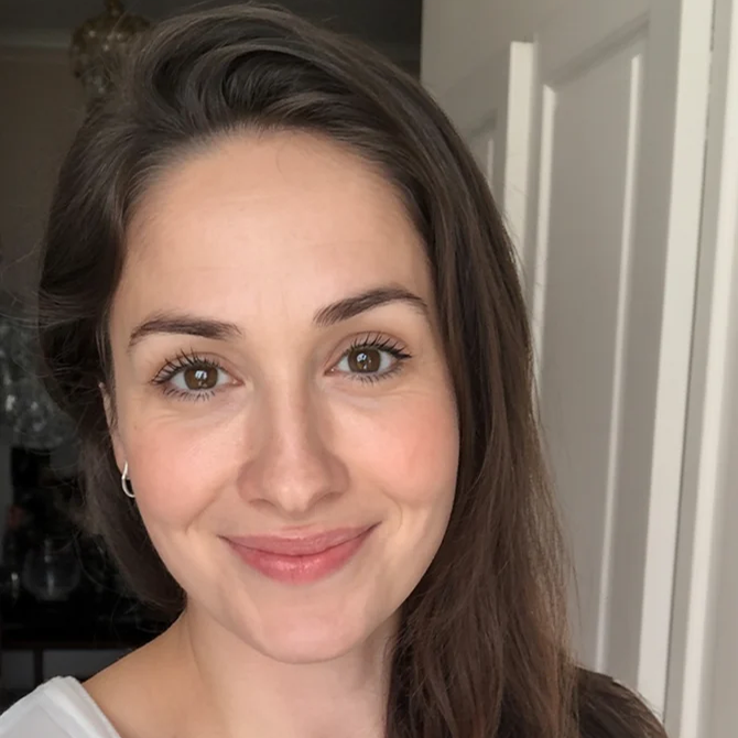 A person smiling indoors with long hair and a white top.