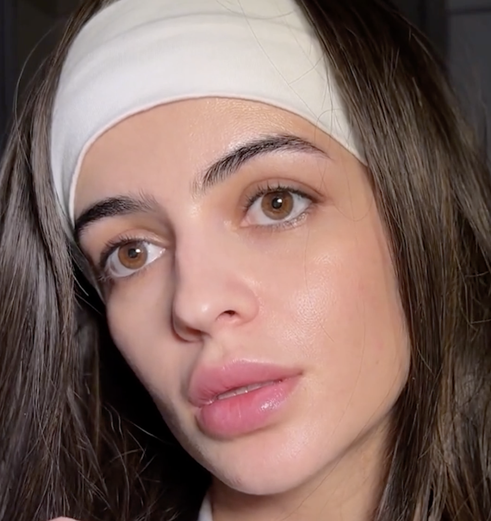 A close-up of a woman with long dark hair, brown eyes, and a white headband on her forehead.