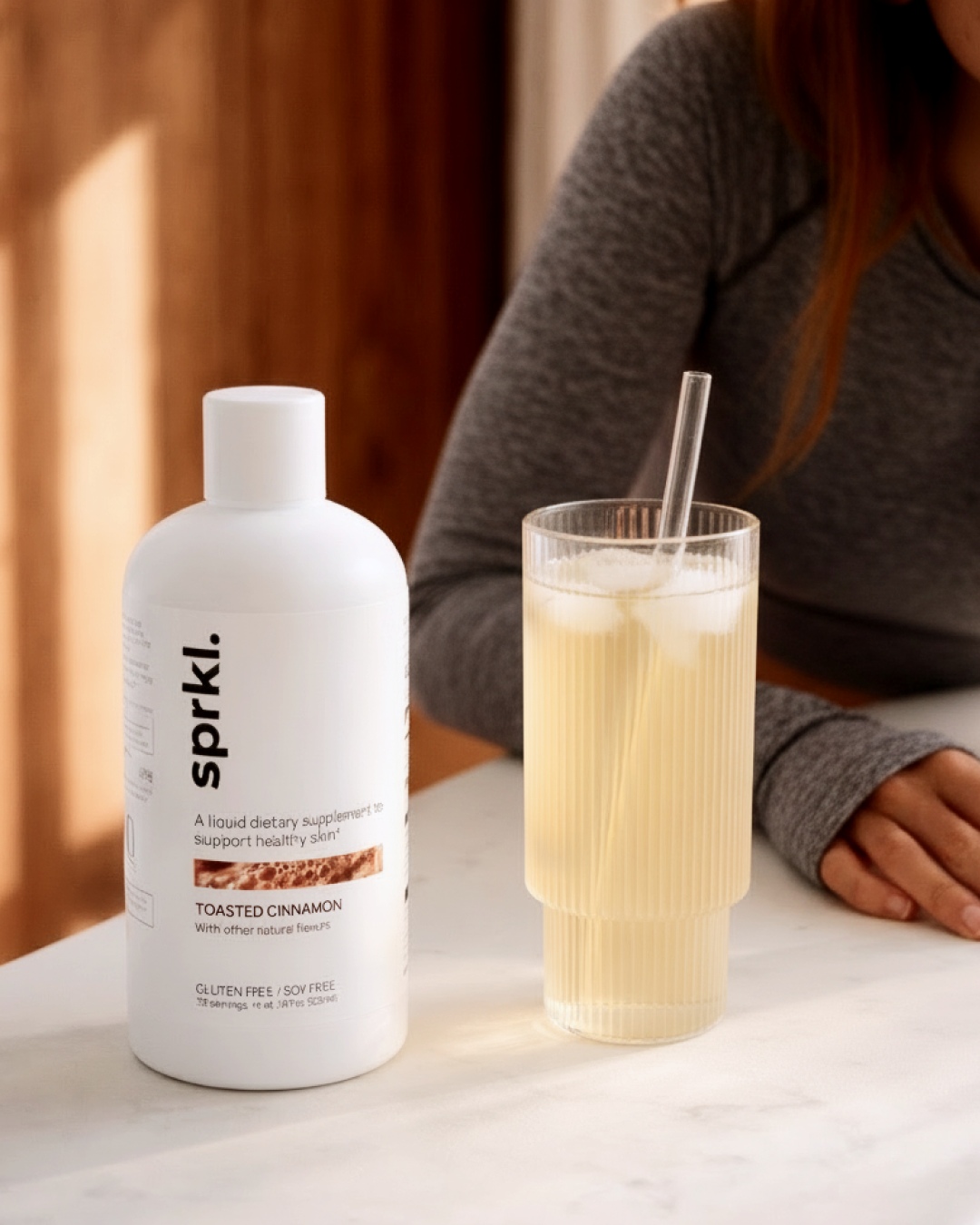 A bottle of Toasted Cinnamon liquid supplement next to a glass of iced drink on a counter.