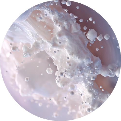A close-up, circular image of a white, milky liquid splashing, creating numerous small droplets and bubbles.