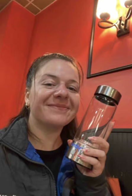Person smiling and holding a clear water bottle indoors.