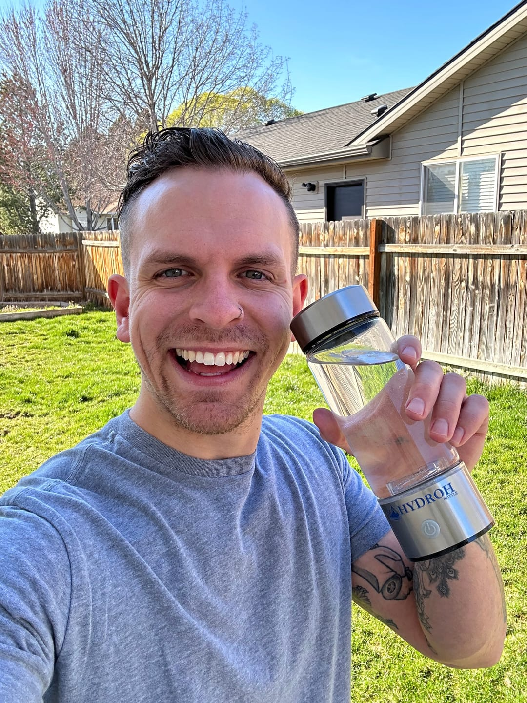 Person smiling outdoors holding a clear water bottle.