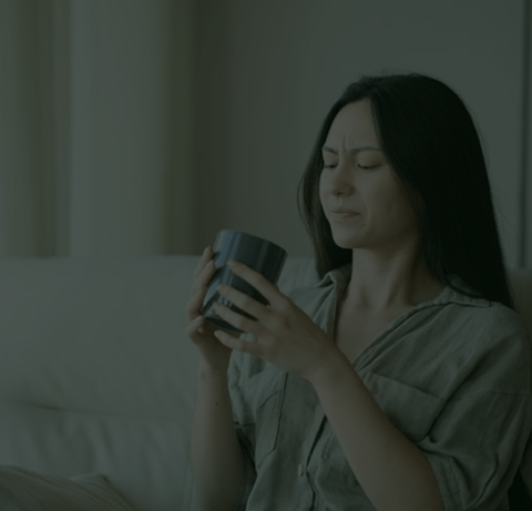 Person sitting on a couch looking at a mug with a thoughtful expression.