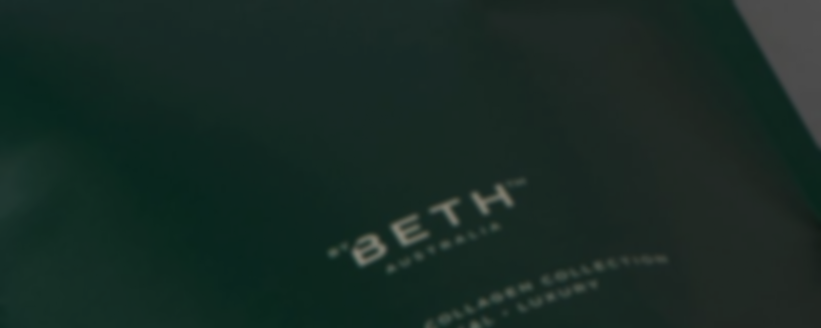 A close-up, soft-focus shot of the 'Beth Australia' logo on a dark green surface.