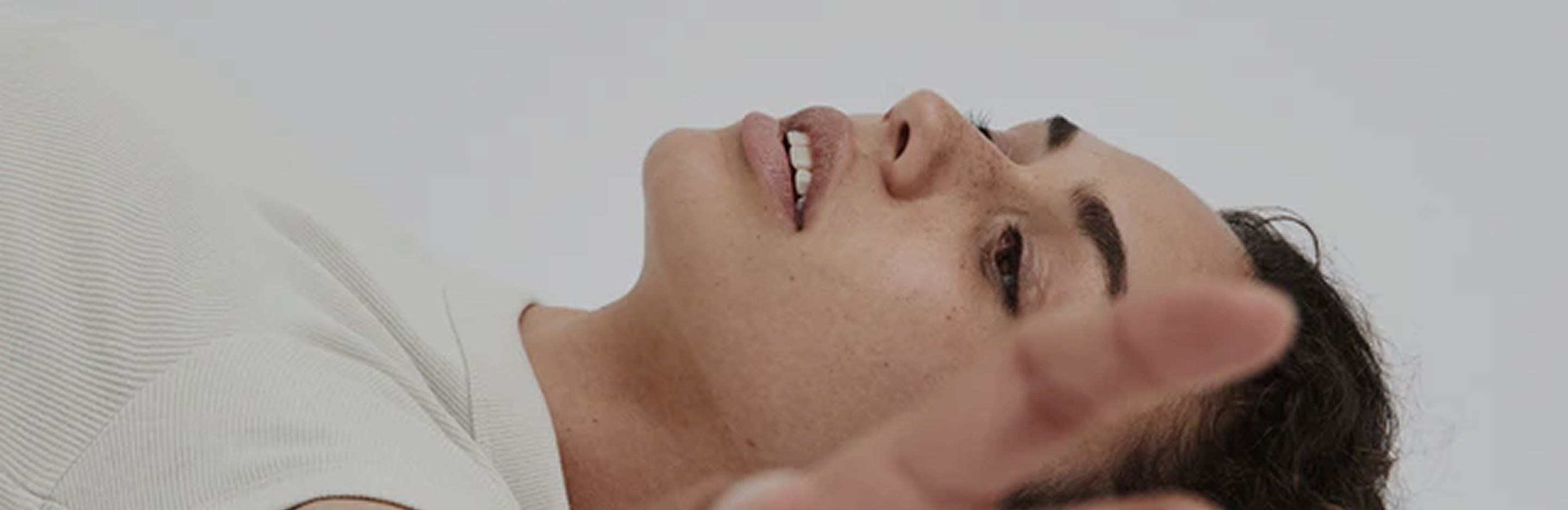A person lying down and looking up, with a blurry hand reaching towards the camera.