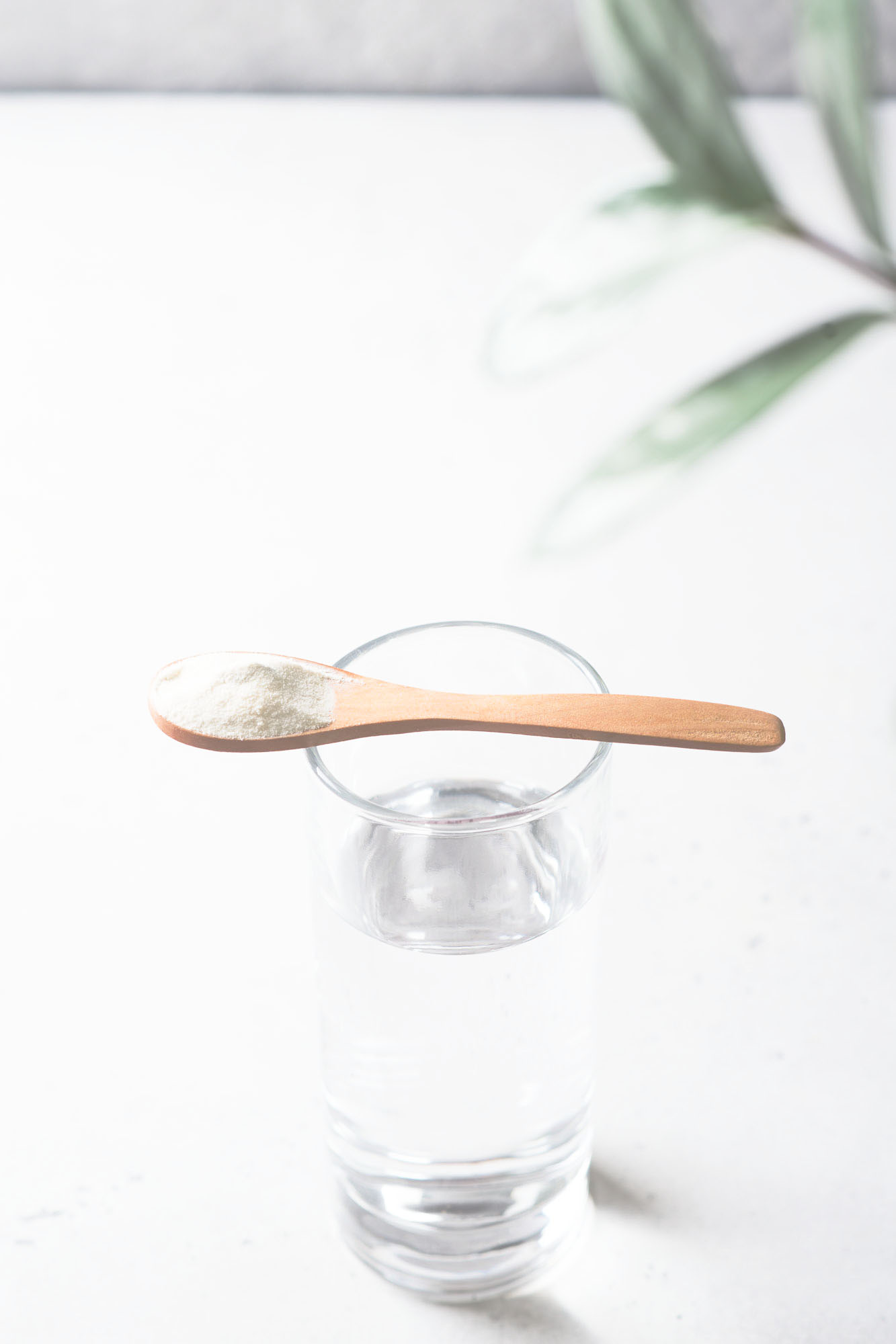 A small wooden spoon with white powder resting on top of a glass of water.