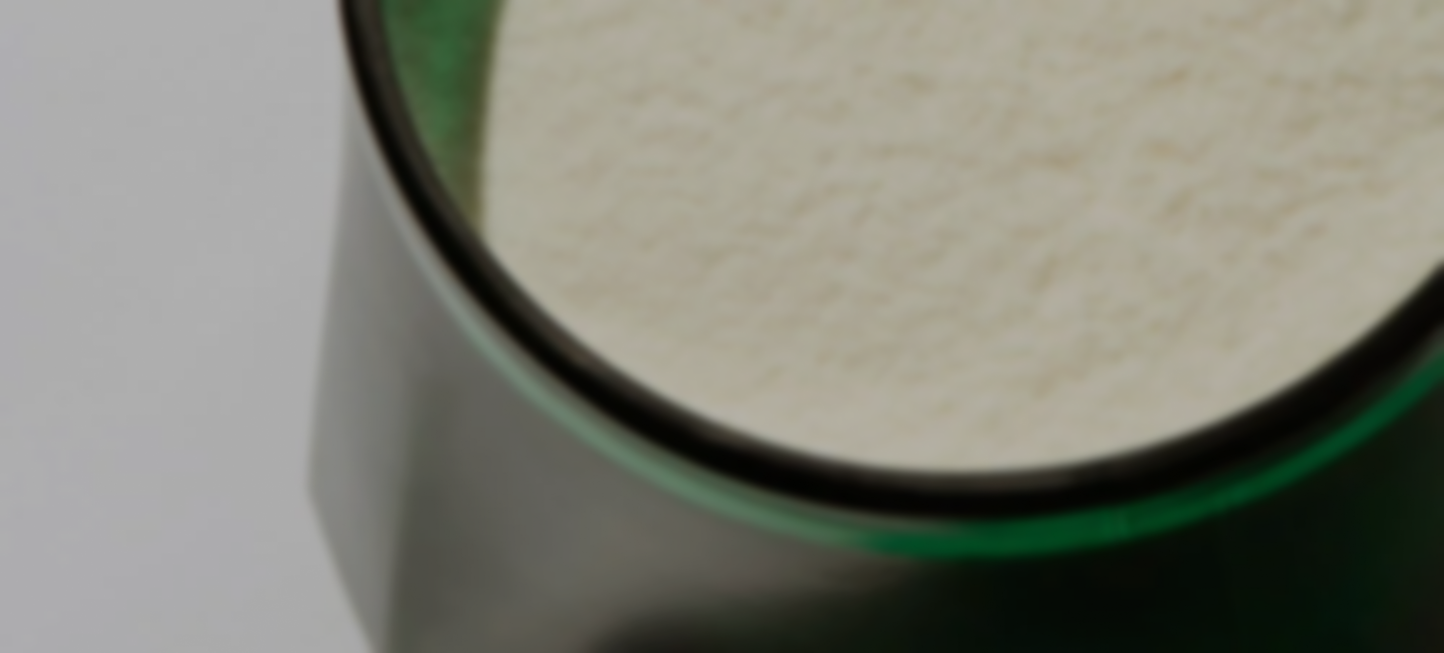 A blurry, close-up photo showing the dark green rim of a container with a light-colored substance inside.
