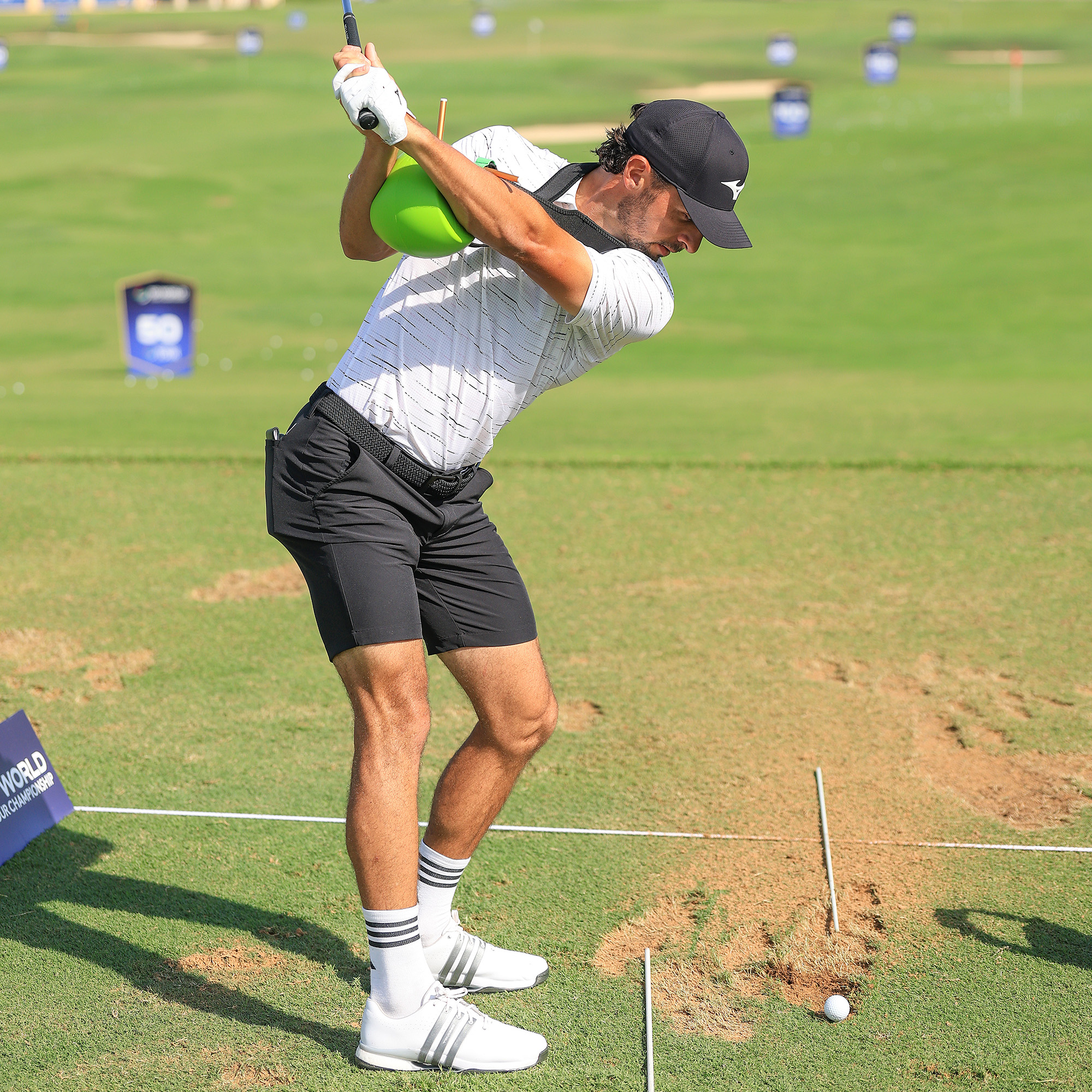 A male golfer practices his swing on a driving range using a green inflatable training aid.