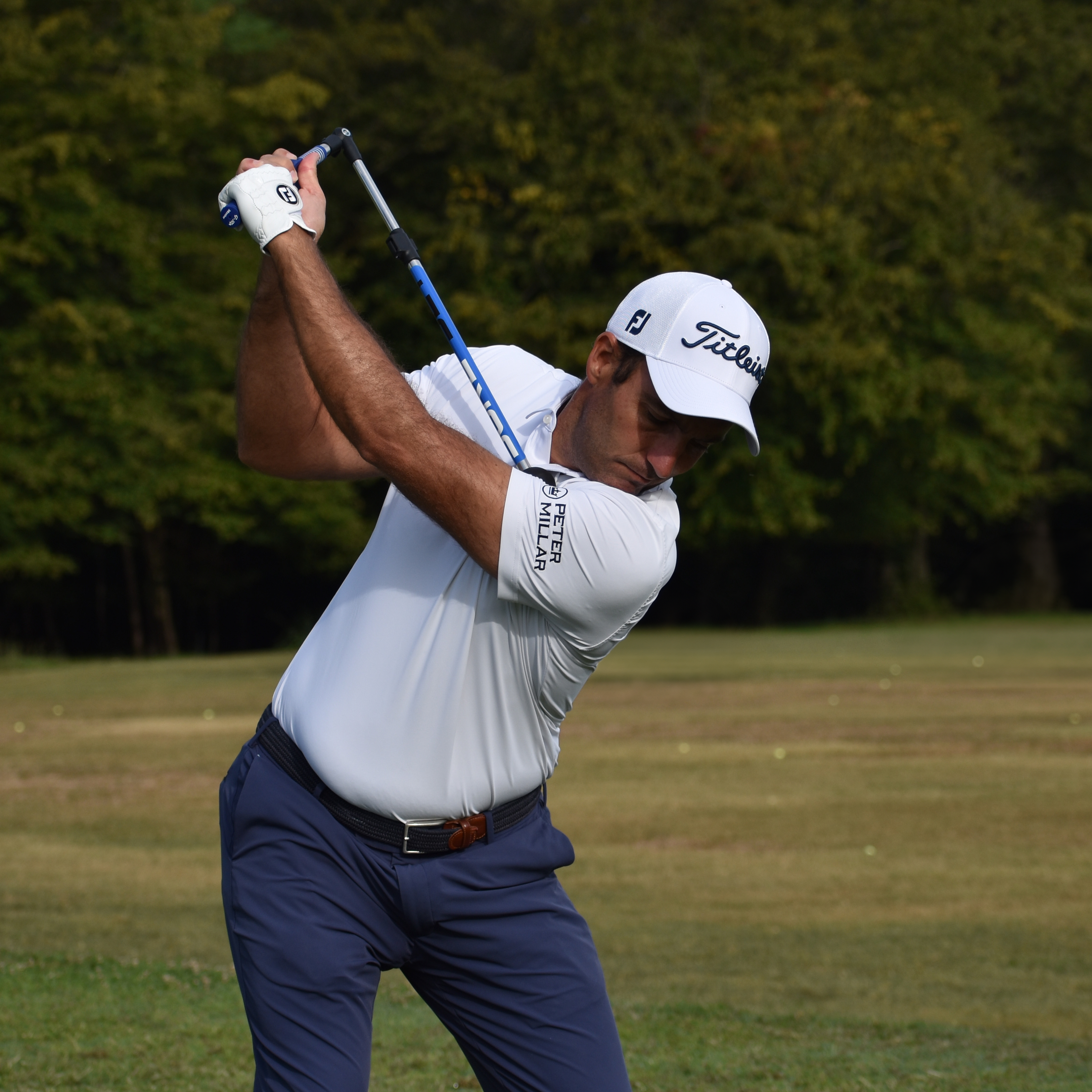 A male golfer wearing a white shirt and Titleist cap is in the middle of his swing.