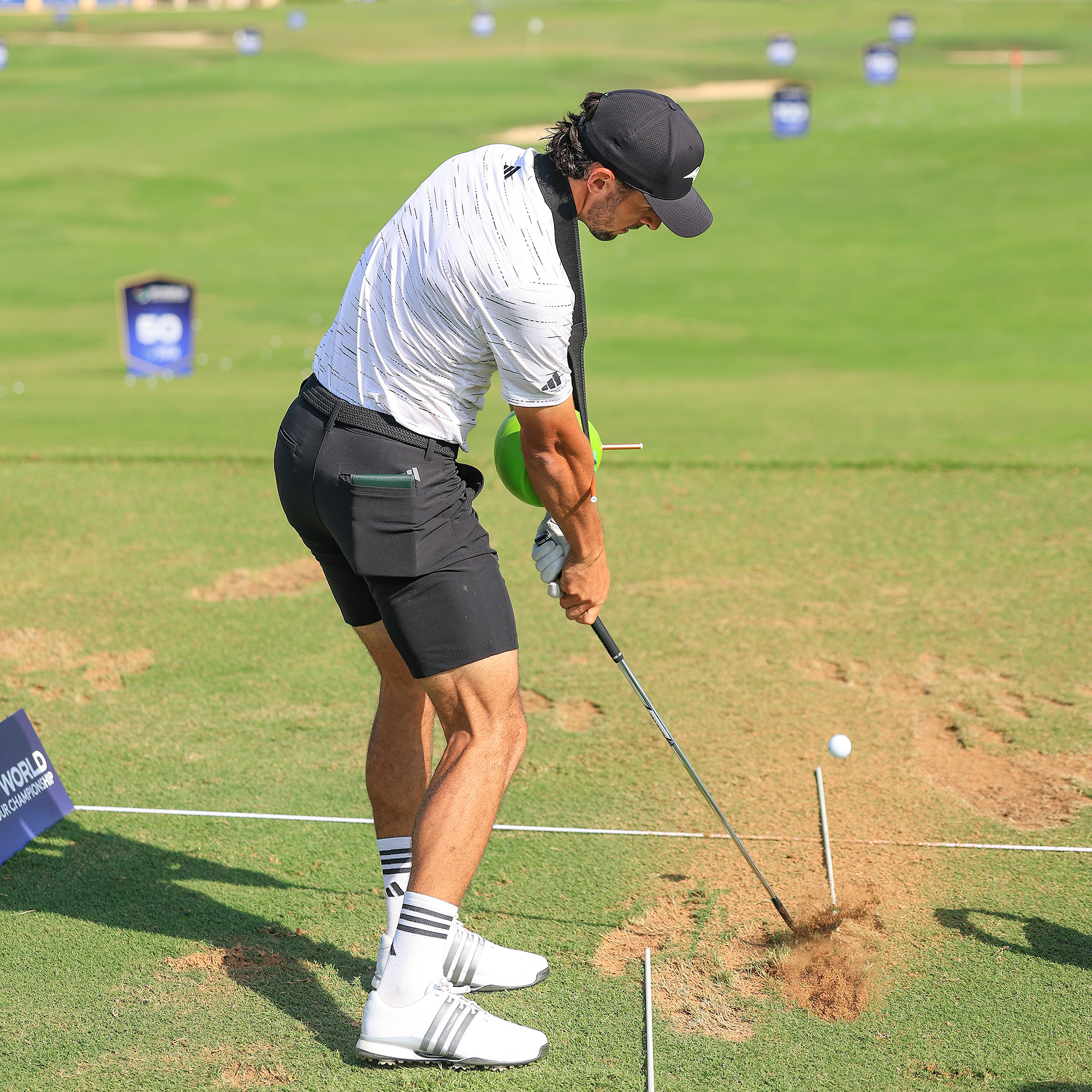 A male golfer practices his swing with a green training aid ball held between his arms.