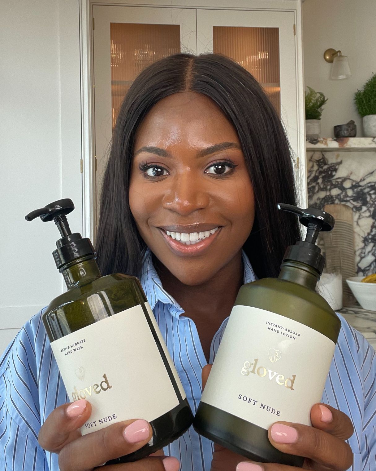 A smiling woman holds two bottles of Gloved hand wash and hand lotion in front of her.