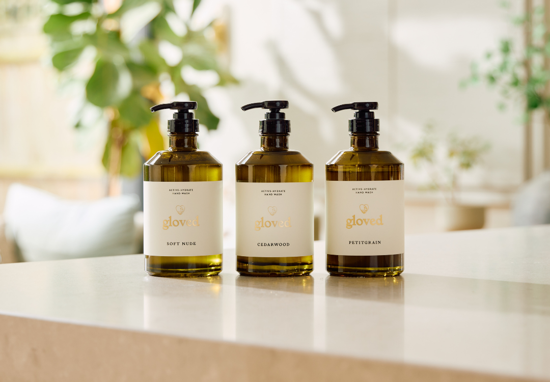 Three pump bottles of Gloved hand wash in different scents, lined up on a countertop.