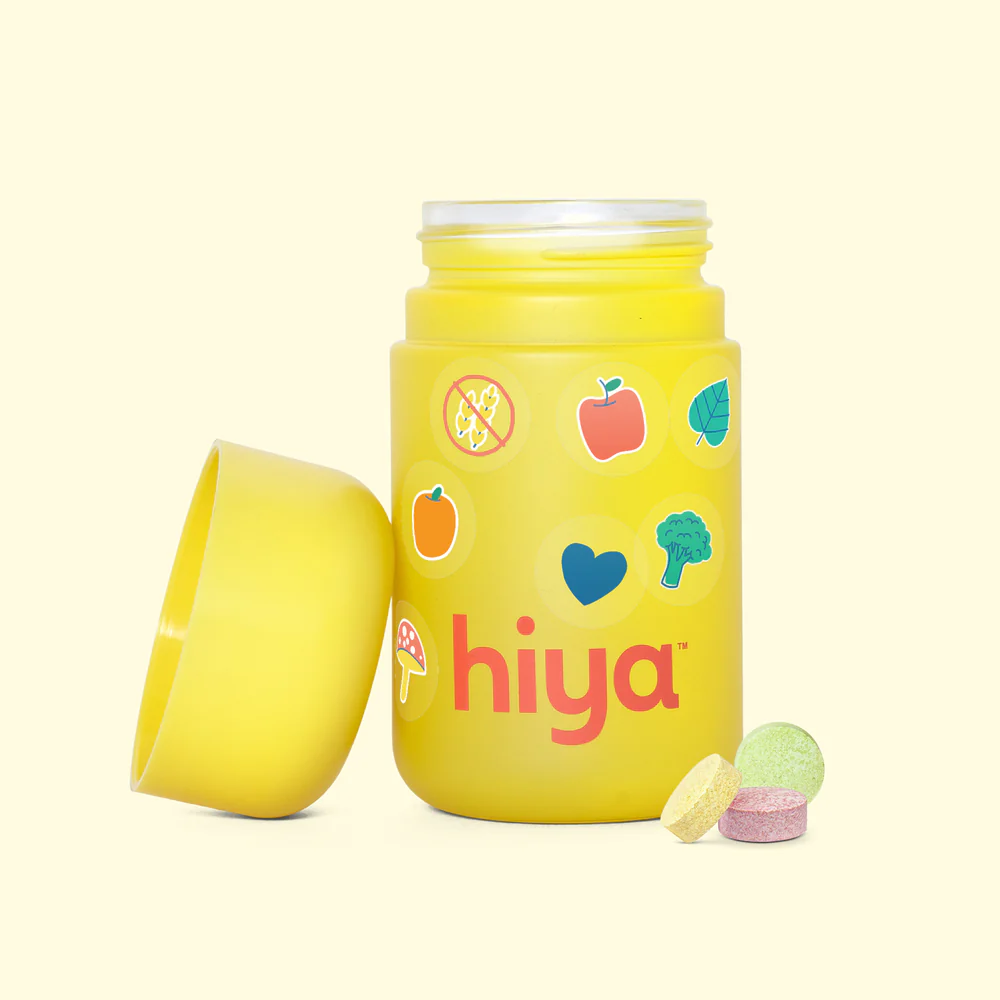A yellow bottle of Hiya vitamins with its cap off and three chewable tablets in front of it.