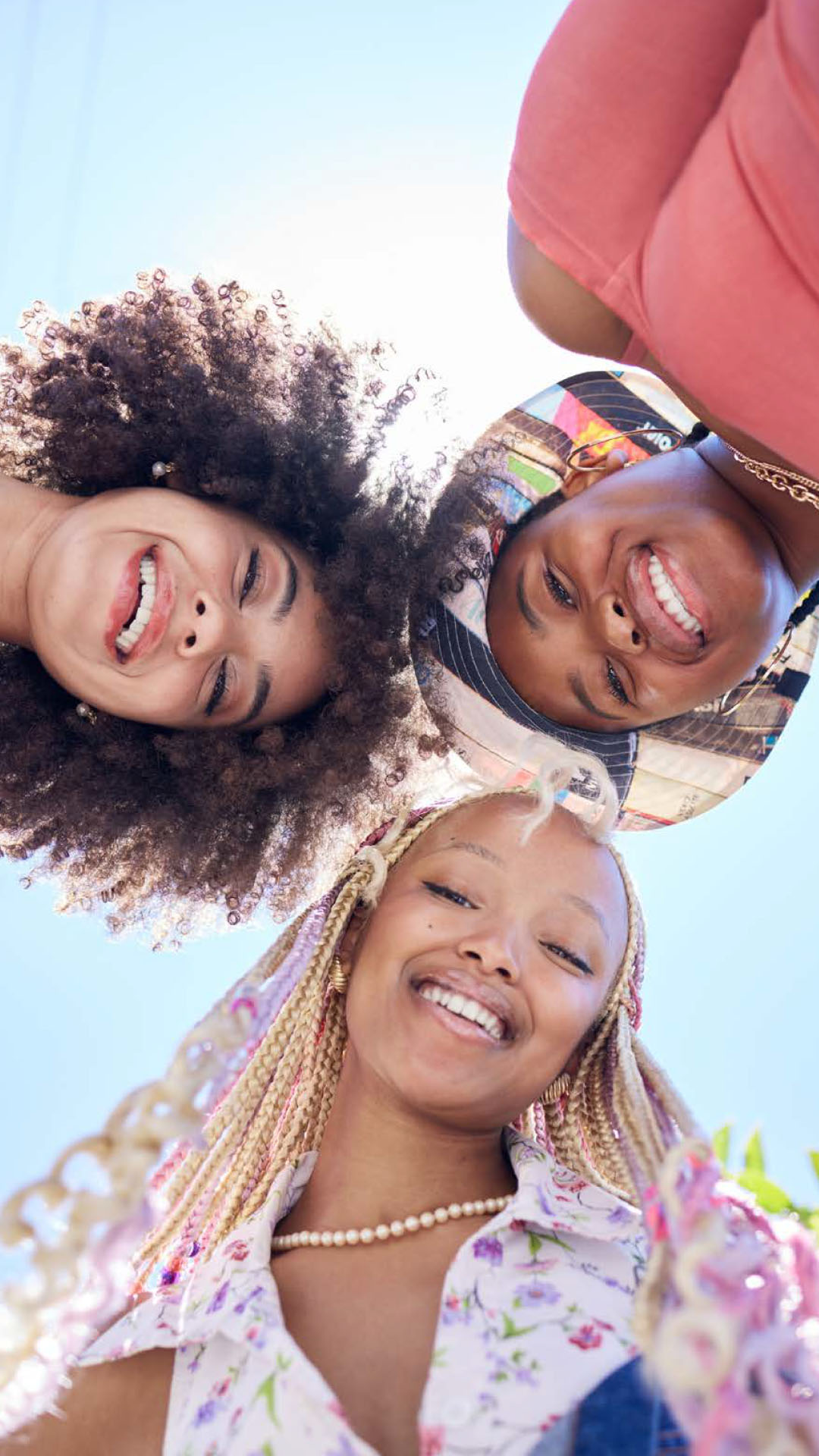 Three people smiling, looking down at the camera against a clear blue sky.