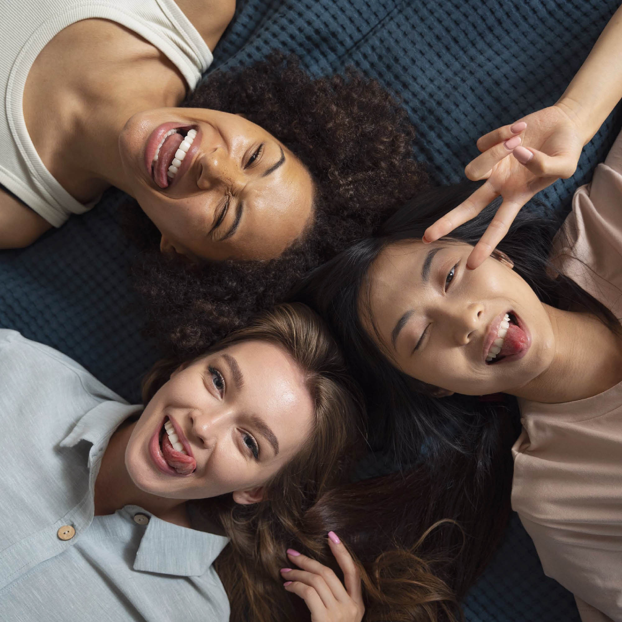 Three people lying on their backs, smiling and making playful faces.