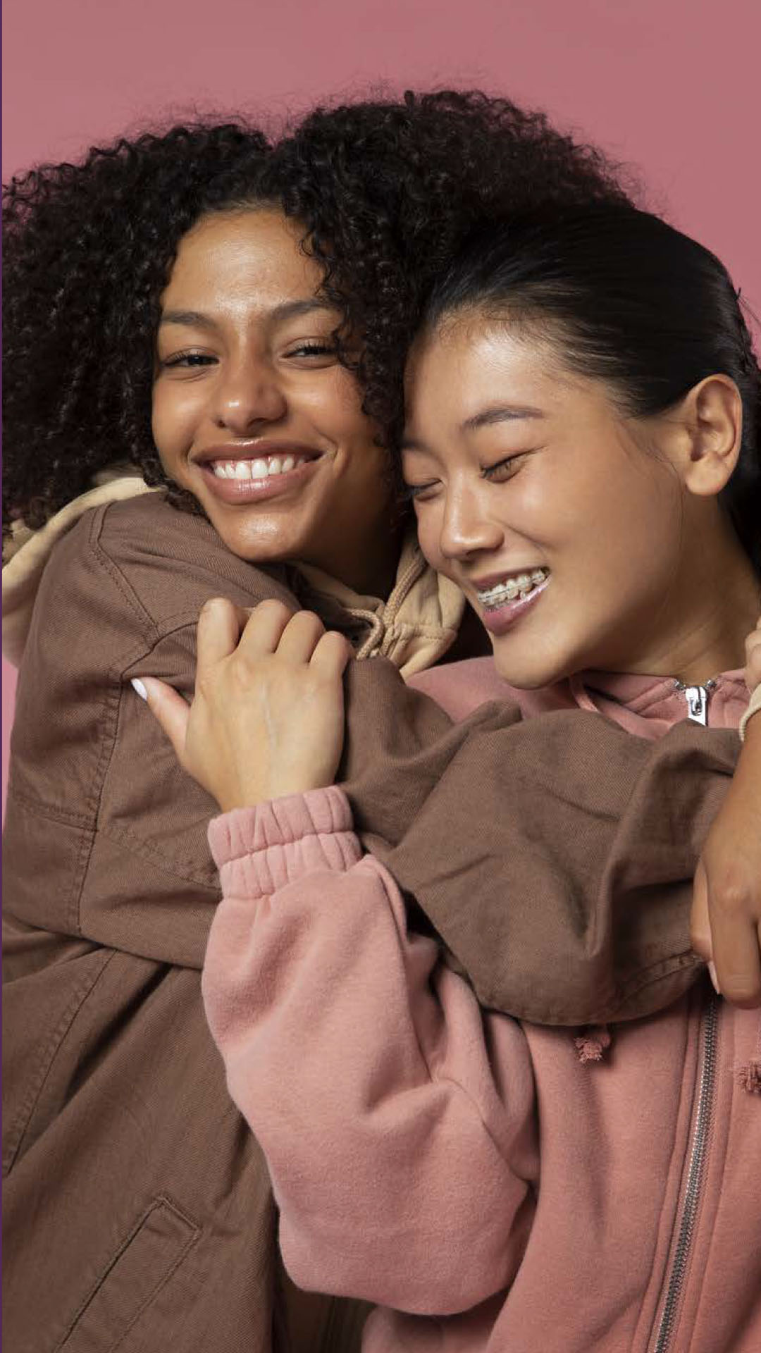 Two people smiling and embracing against a pink background.