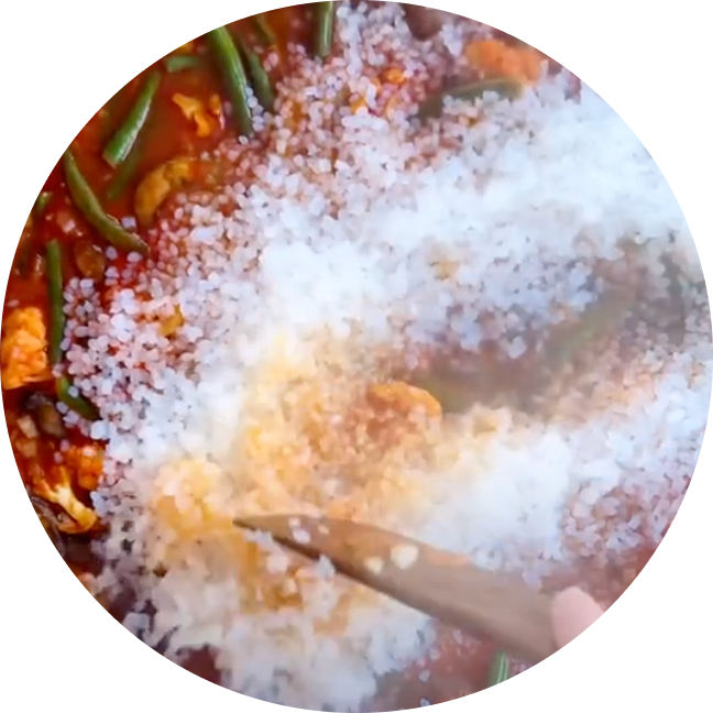 Cooking with rice and vegetables in a pan, stirred with a wooden spoon.