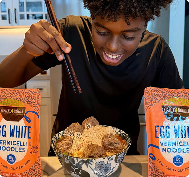 Person eating noodles with chopsticks between two noodle packages.