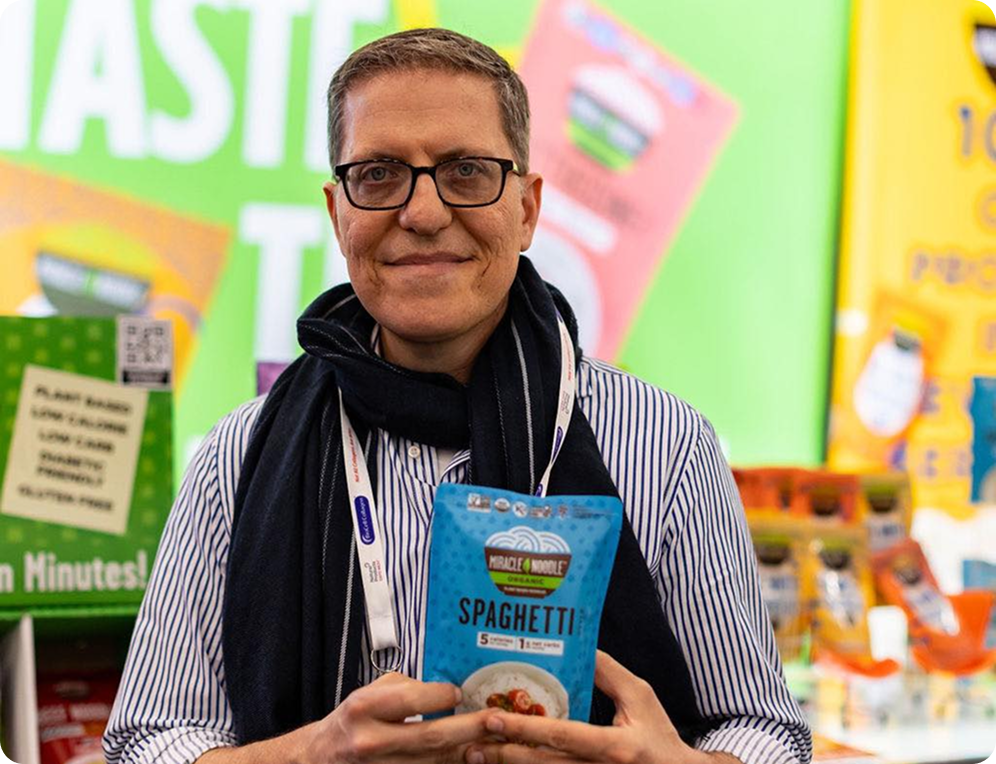 Person holding a packaged spaghetti product against a colorful background.
