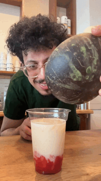 Person pouring liquid from a coconut into a cup with red and white layers.