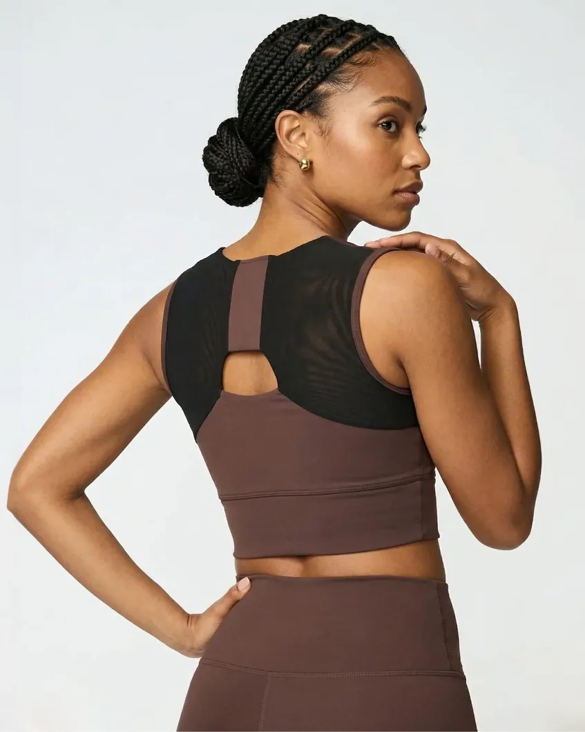 Back view of a woman in a brown sports bra with a black mesh panel and keyhole cutout.