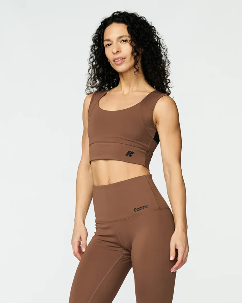 A woman with long curly hair wearing a matching brown sports bra and high-waisted leggings.