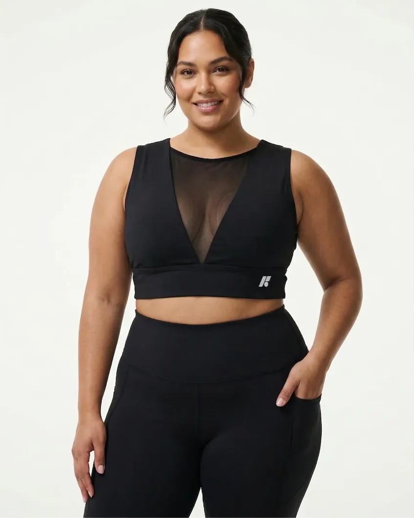 A woman models a black sports bra with a sheer V-neck panel and matching black leggings.