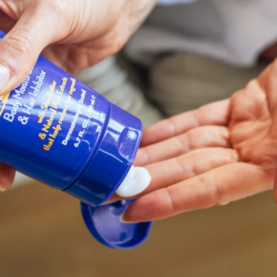 A person squeezes a white lotion from a blue tube into their open palm.
