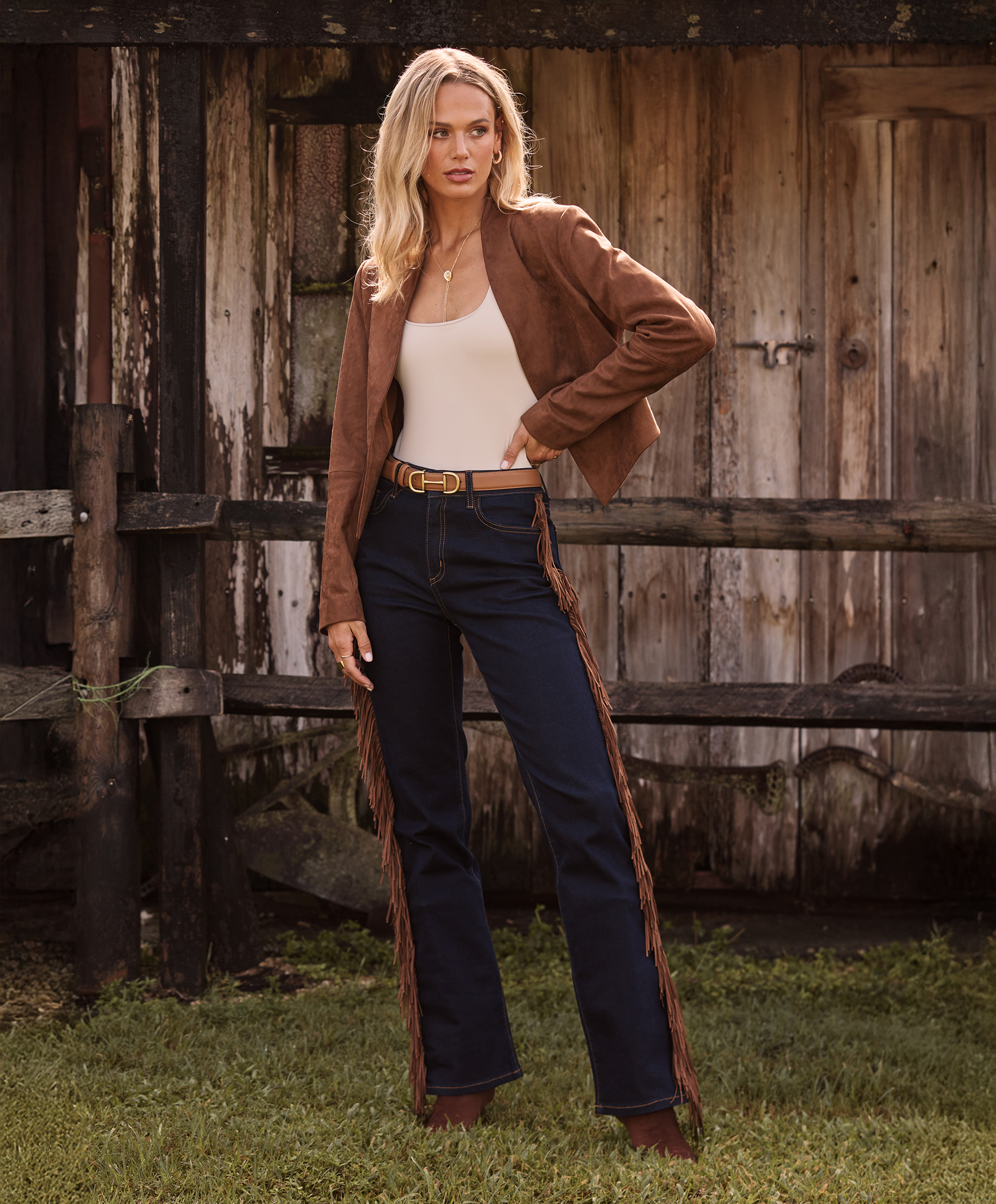 Person in fringe pants and jacket standing by a wooden fence.