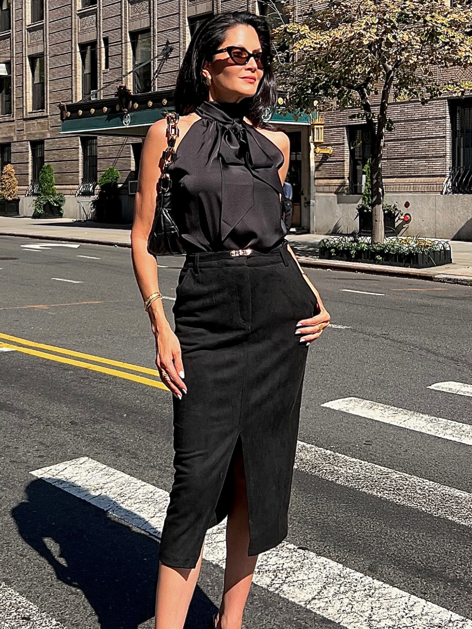 Woman in black outfit standing on a city street with buildings in the background.