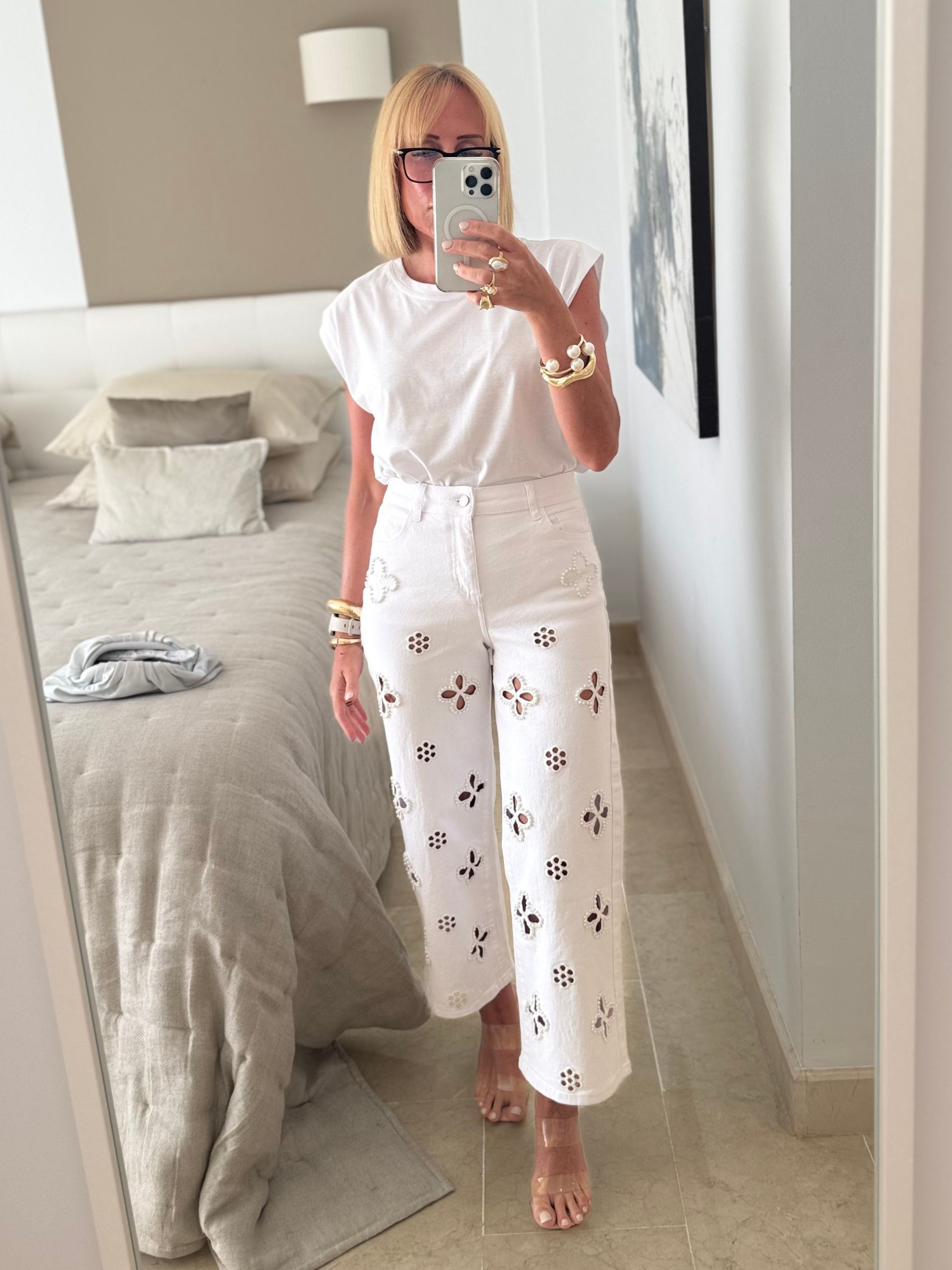 Person taking a mirror selfie wearing a white outfit with floral cutouts.