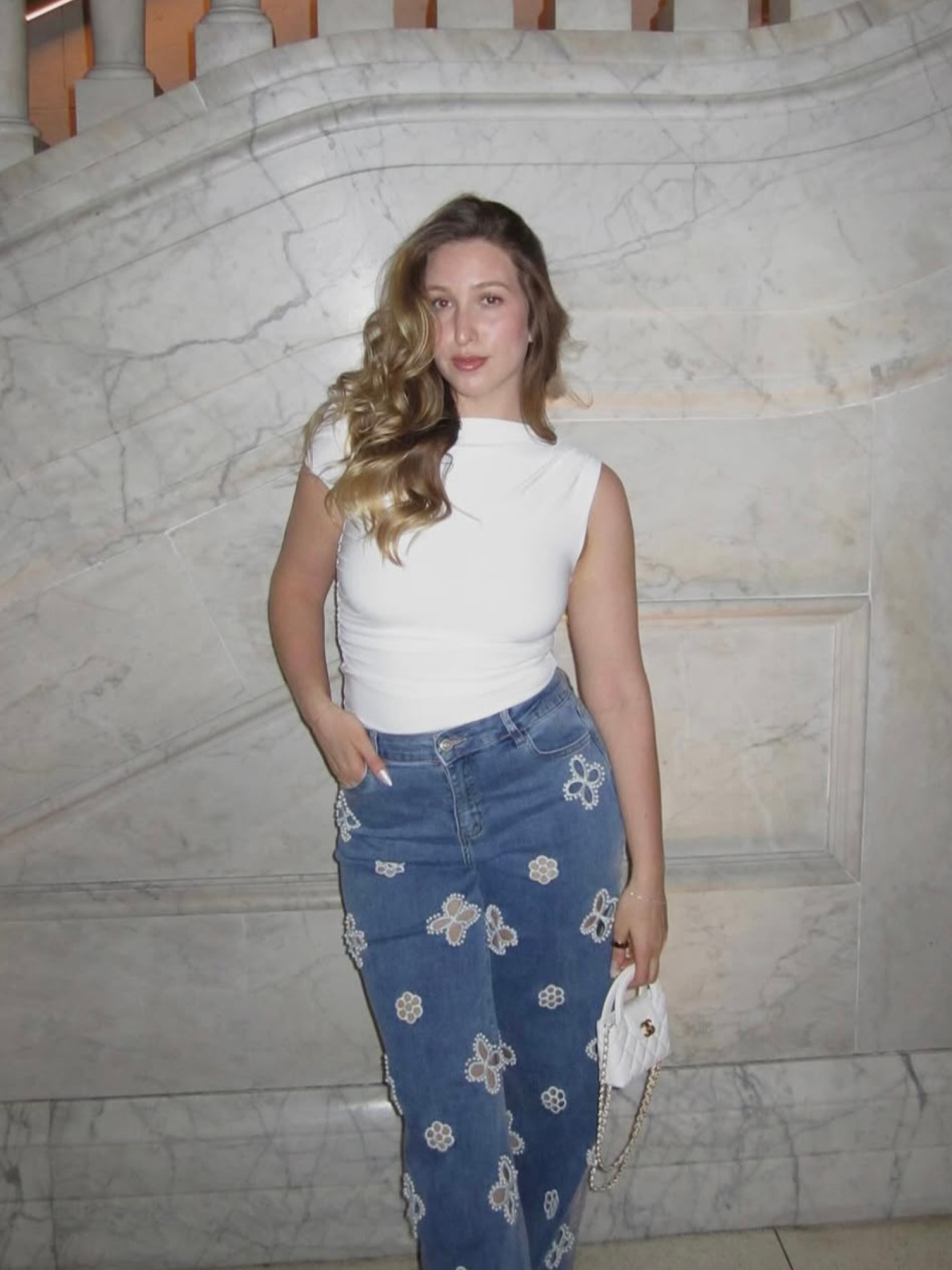 Woman in white top and floral jeans standing outdoors with ocean view.