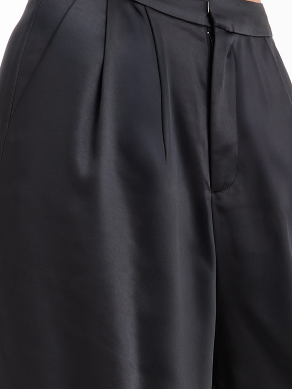 Close-up of black satin pants with pleats.