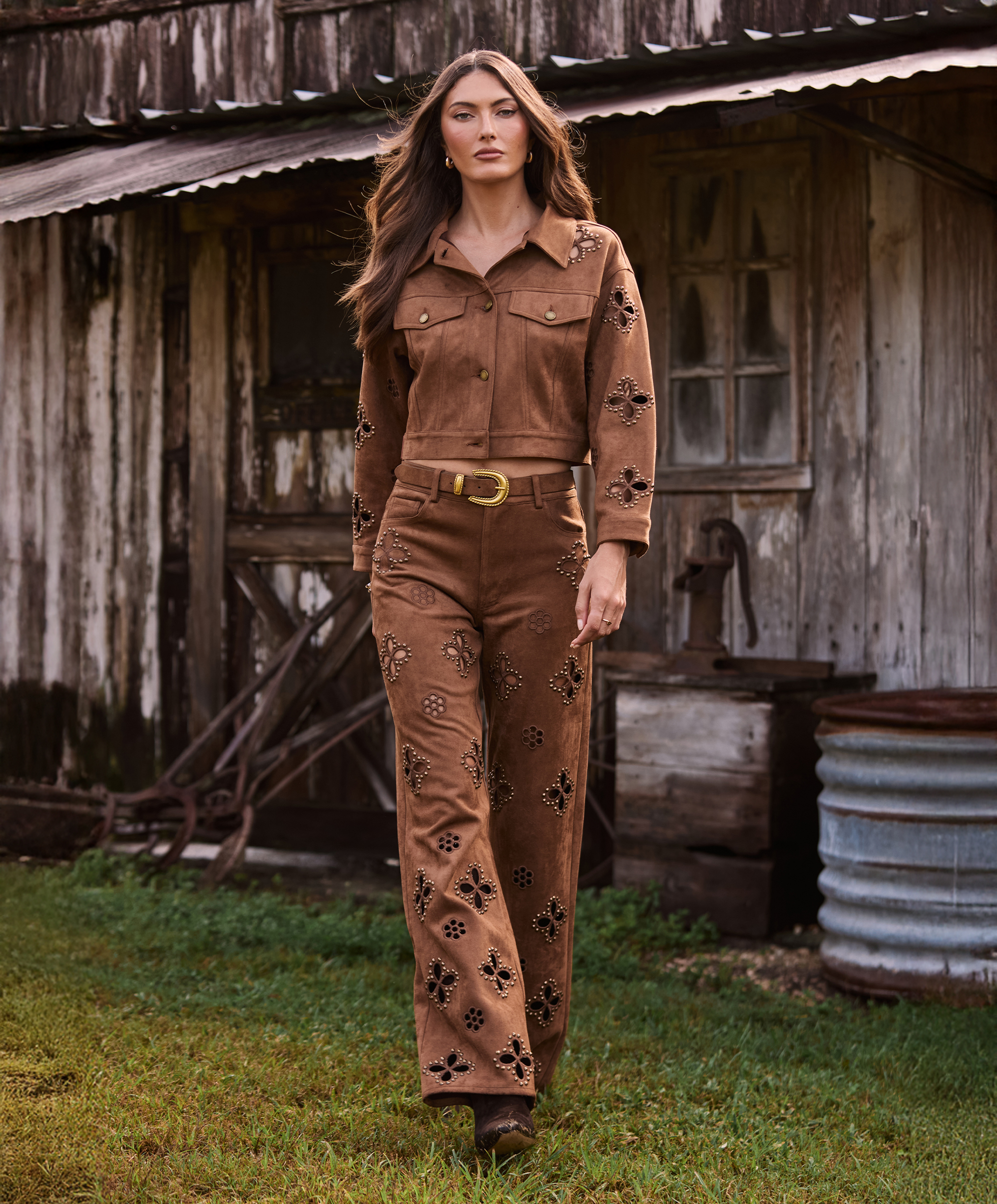 Woman in brown embroidered outfit standing in front of a rustic wooden building.