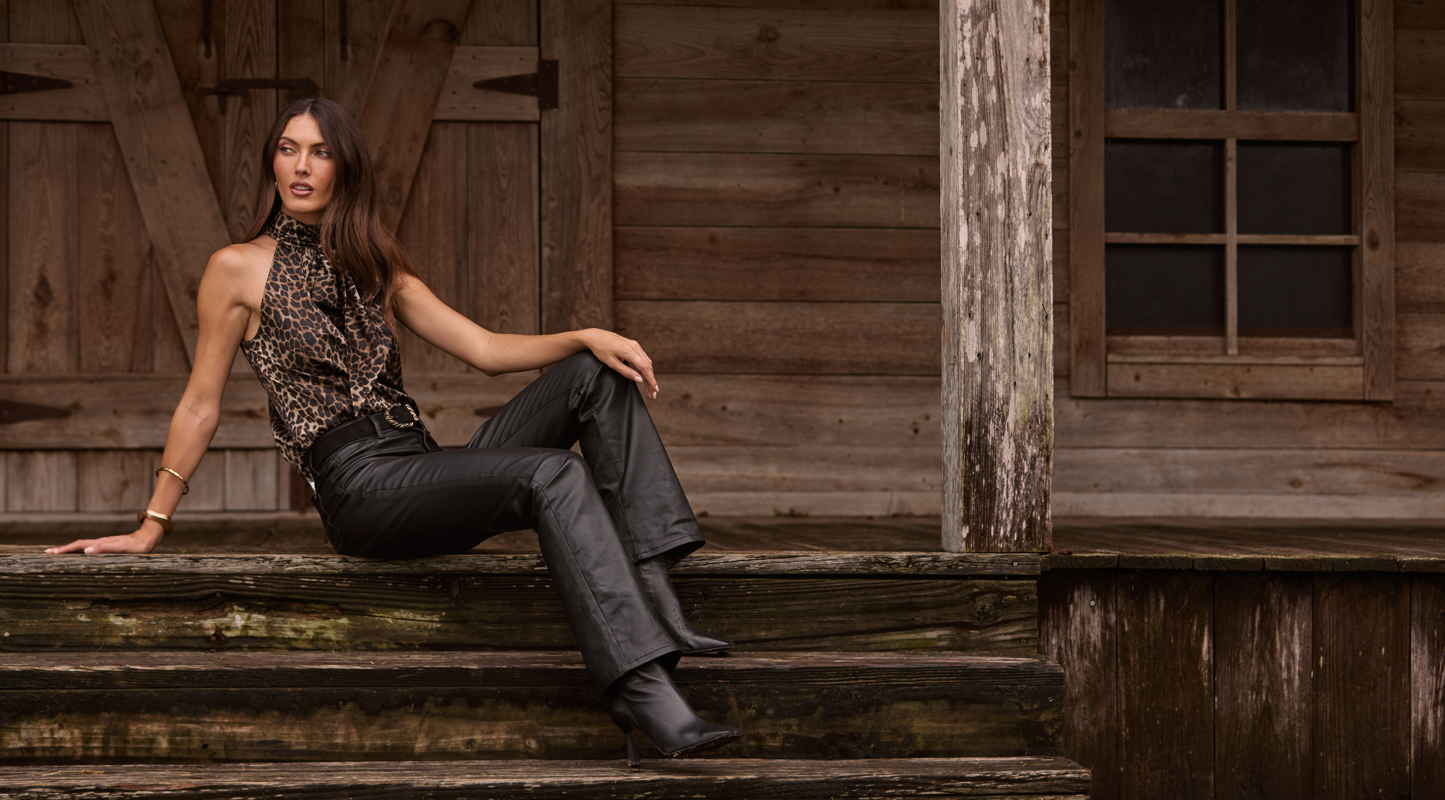 Person sitting on wooden steps, wearing leopard print top and black leather pants.
