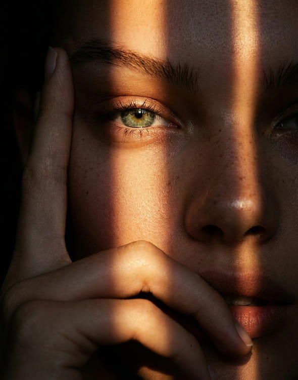 A close-up of a person's face with green eyes, with vertical stripes of light and shadow across it.