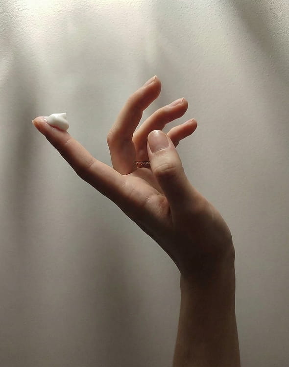 A close-up of a hand holding a dollop of white cream on the tip of the index finger.