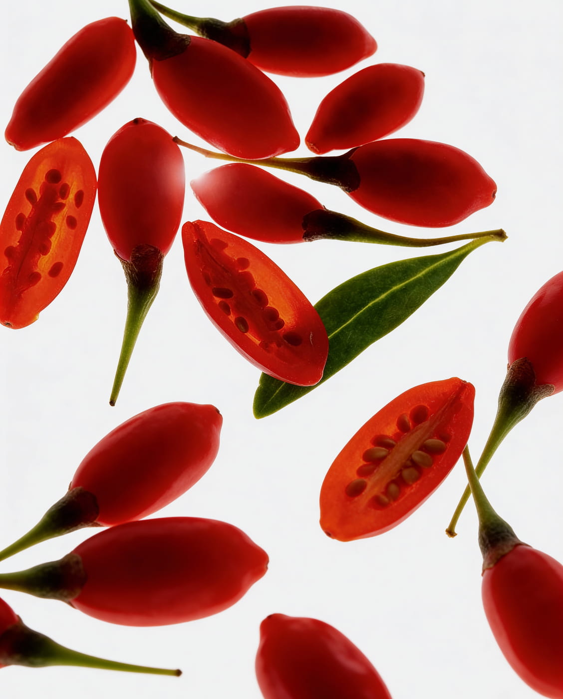 A close-up shot of whole and sliced goji berries with a leaf, against a white background.