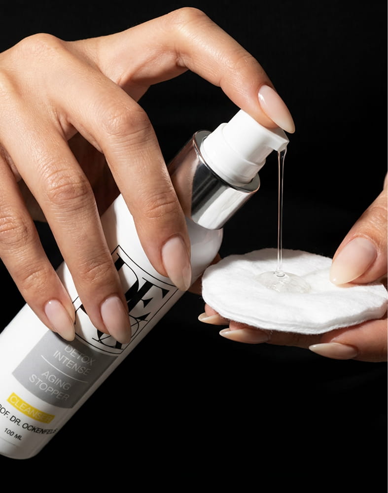 A person dispenses a clear liquid from a pump bottle onto a round cotton pad.