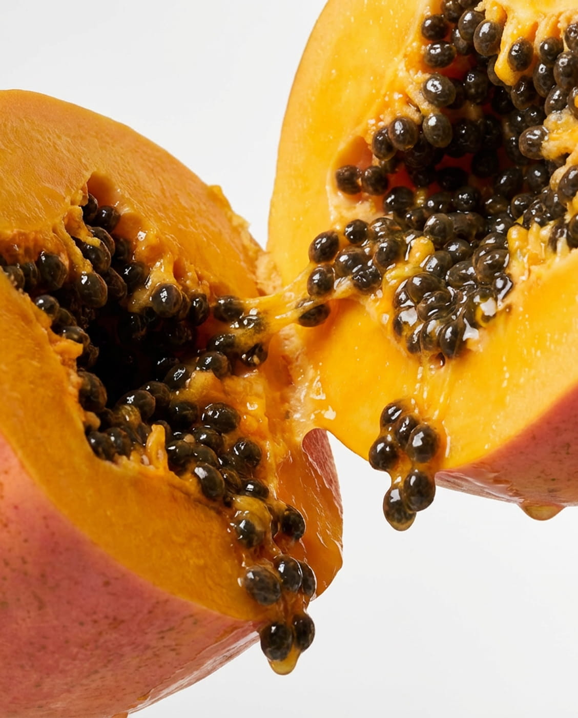A close-up of a ripe papaya cut open, revealing its orange flesh and shiny black seeds.