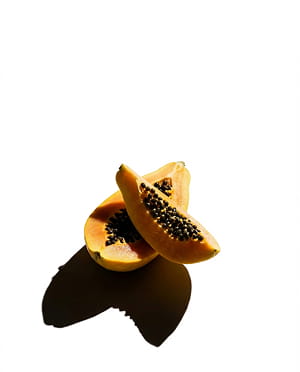 Two wedges of ripe papaya with black seeds, casting a hard shadow on a white background.